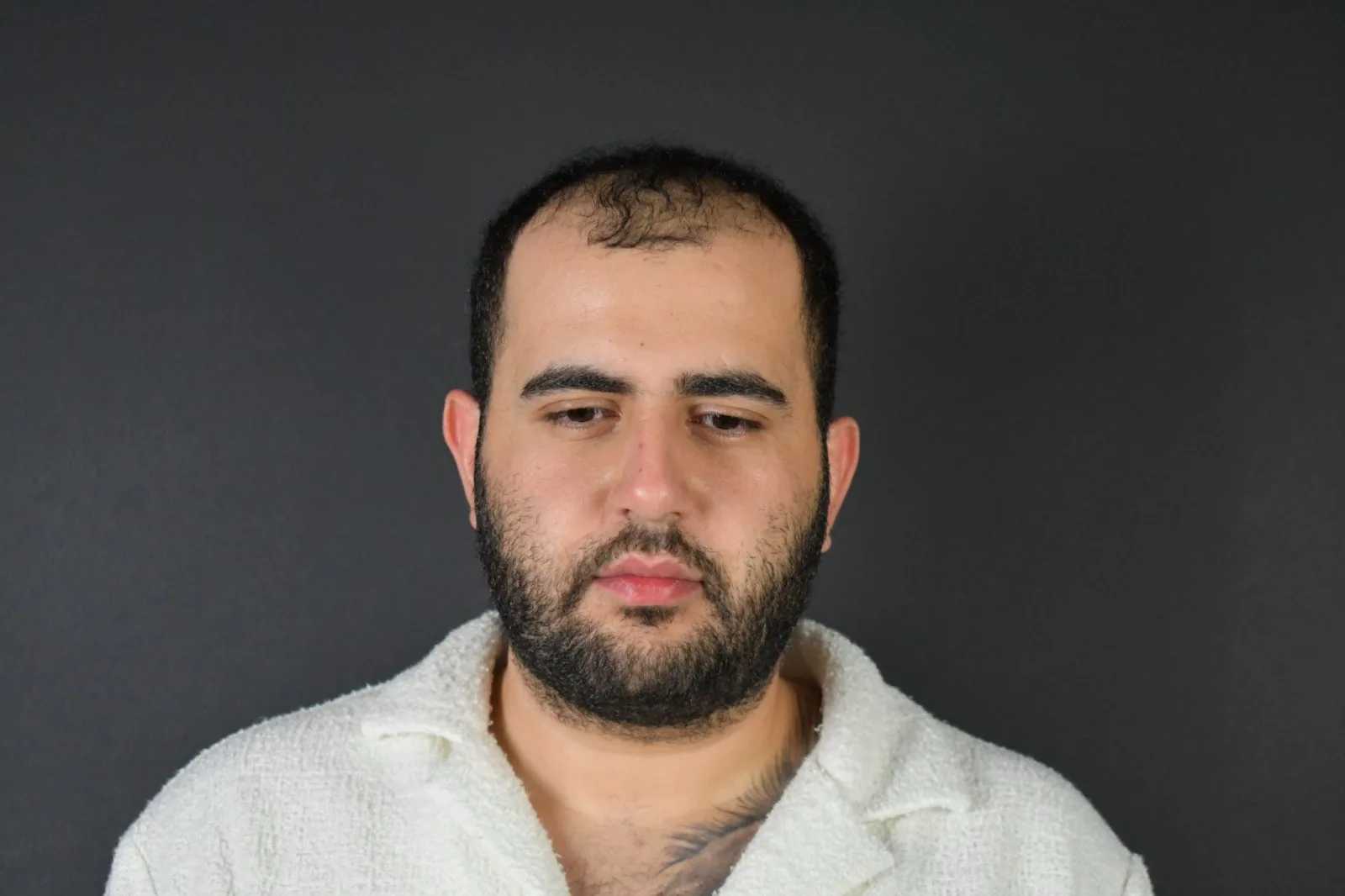 Man with beard wearing light-colored shirt against dark gray background